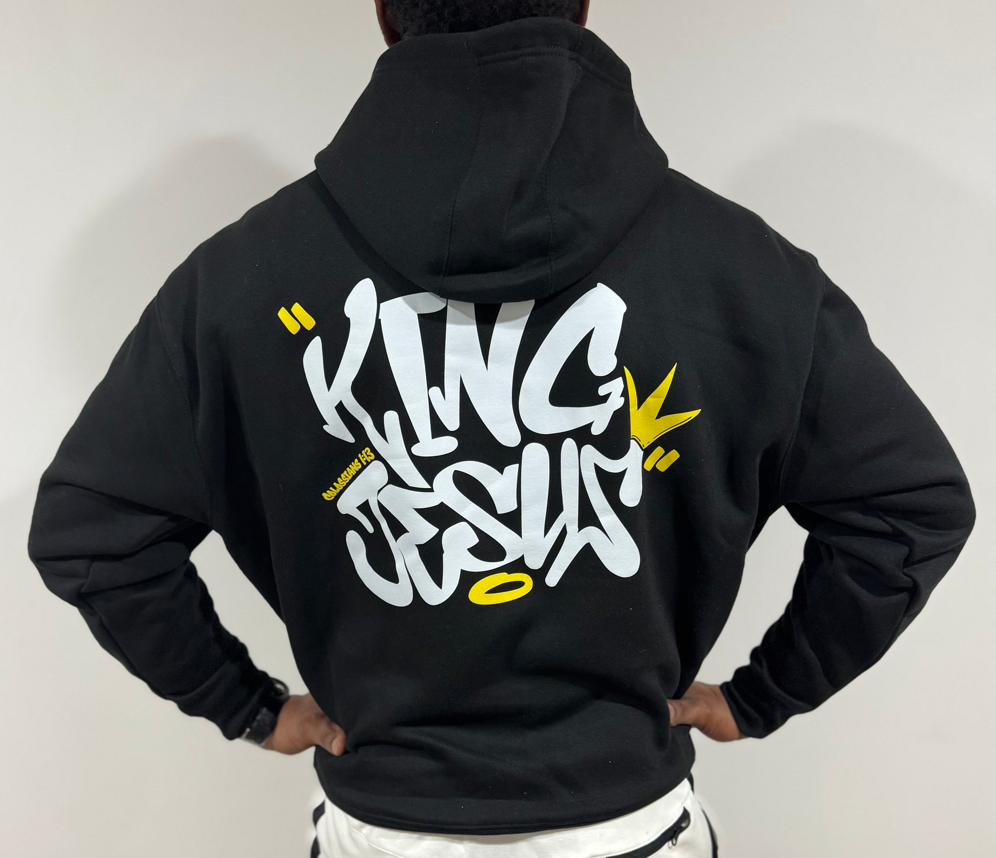 African American man standing with hands on his waist, showcasing the back design of the King Jesus Hoodie—bold Christian streetwear with a faith-inspired message.