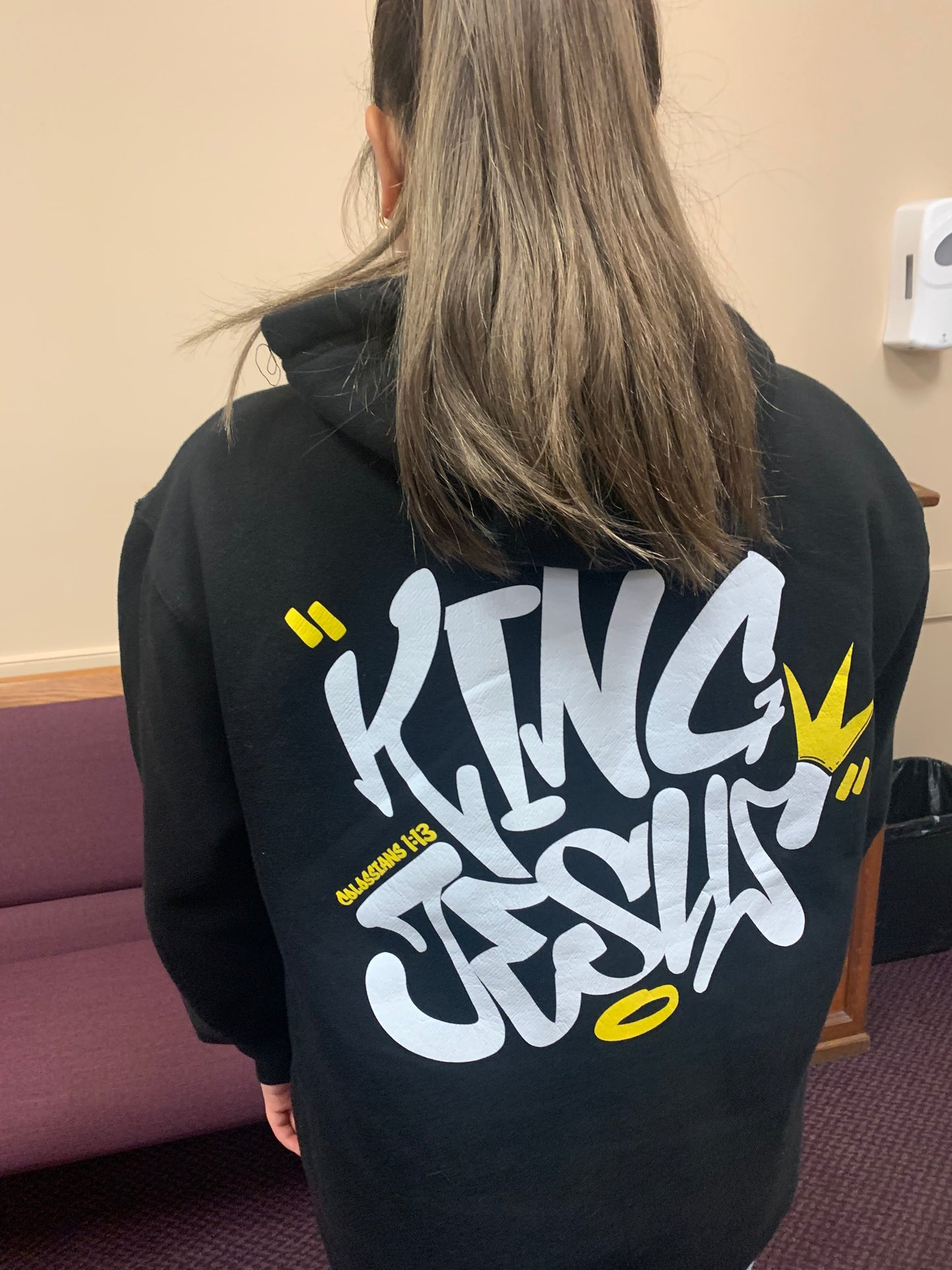 Woman with long hair facing away, showcasing the back design of the King Jesus Hoodie—Christian streetwear with bold faith-inspired style.