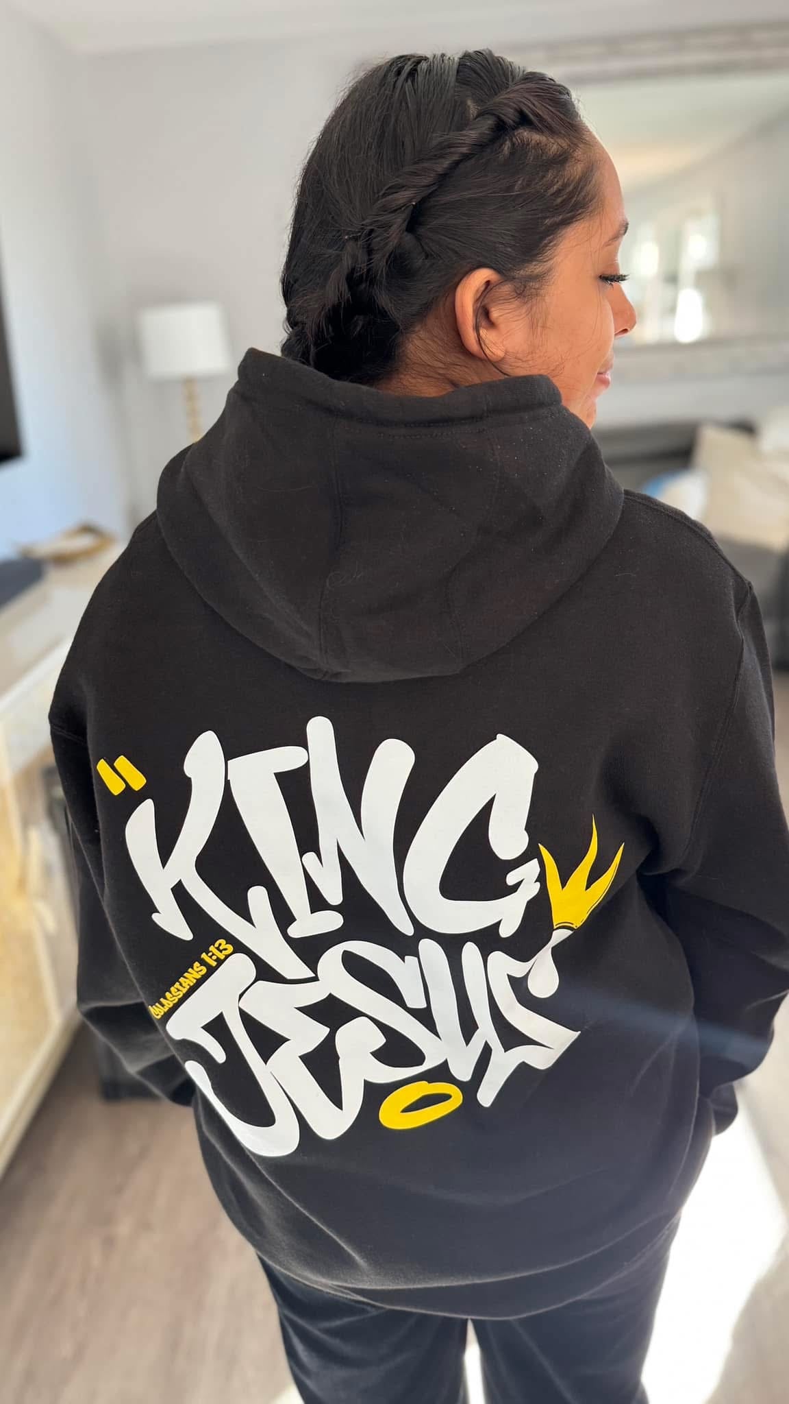 Smiling woman partially showing her face while displaying the back design of the King Jesus Hoodie—Christian streetwear with a bold faith statement.