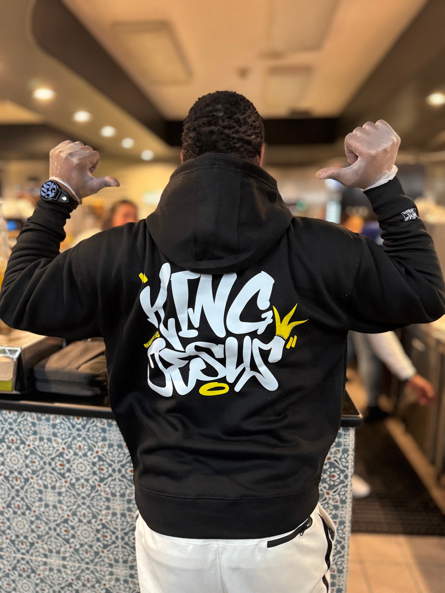 African American man in full color, showing the back of the King Jesus Hoodie with hands up and thumbs pointing at the design—bold Christian streetwear with a faith-inspired message.